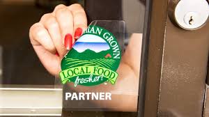 Hand pressing a clear window cling with a green local food partner logo onto a glass door